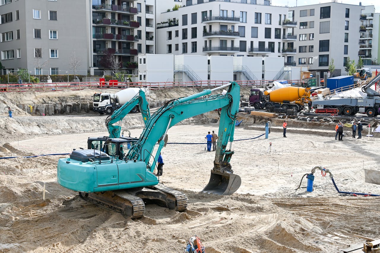 gallery-4 A busy construction site with machinery, workers, and residential buildings in the background.