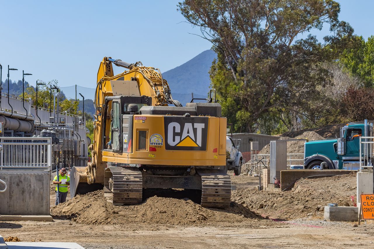 services-01 Excavator working at a construction site with mountains in the background.