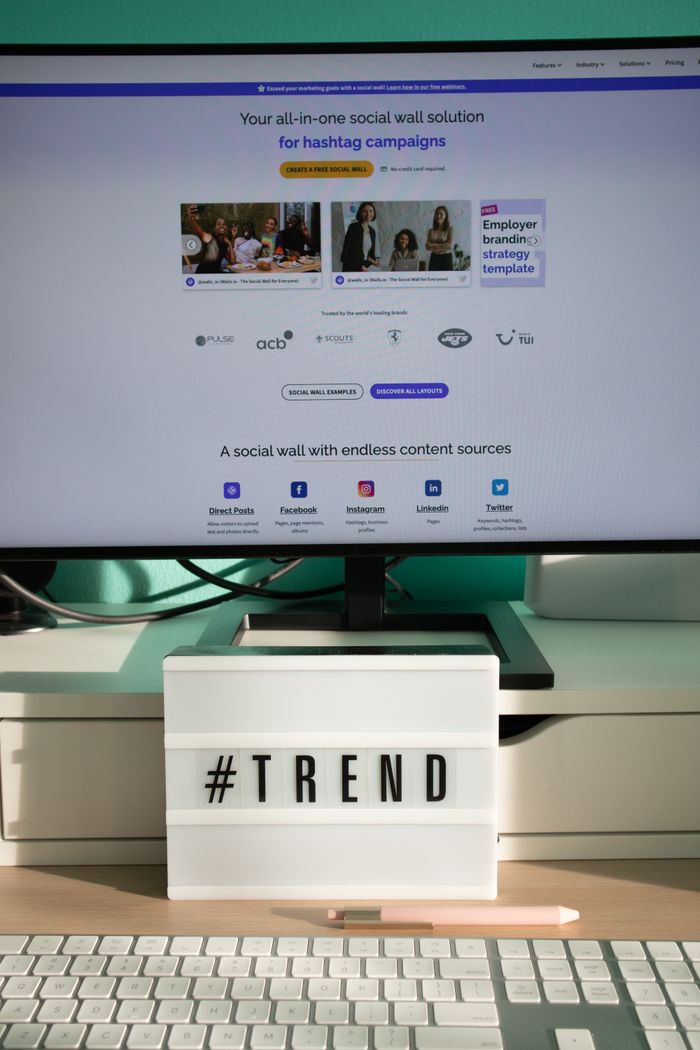 services-01 A clean and modern desk setup with a lightbox displaying '#TREND' and a computer monitor showing a social wall solution.