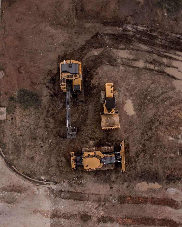 about-img An aerial shot of heavy machinery at a construction site, including excavators and road rollers.