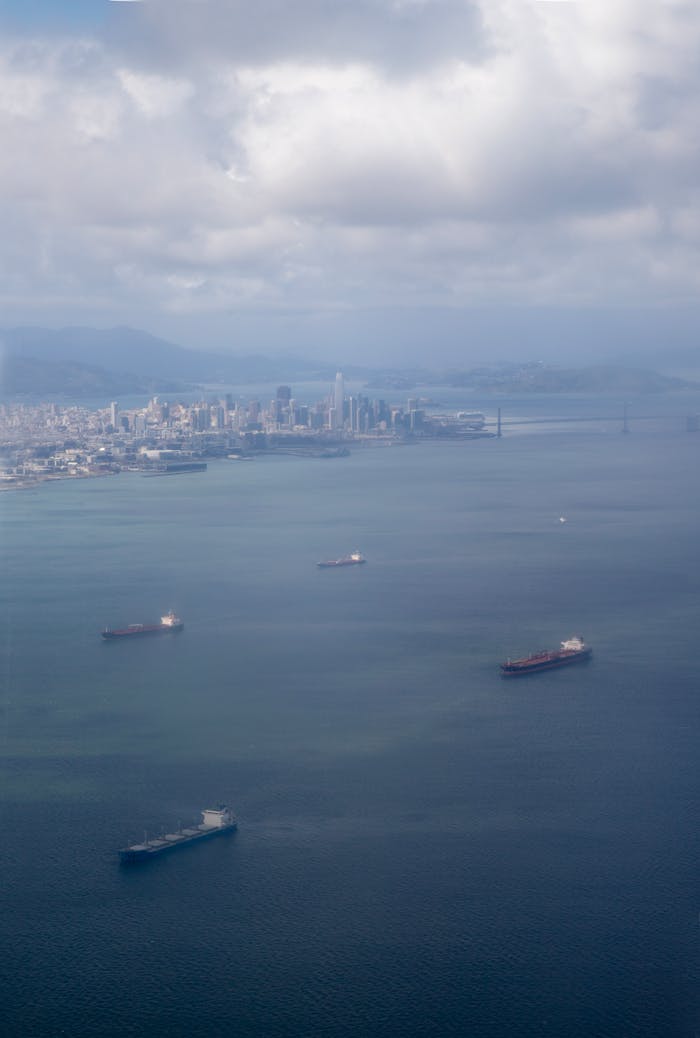 ours-journey Aerial shot of cargo ships in San Francisco Bay with city skyline and iconic bridge in the background.