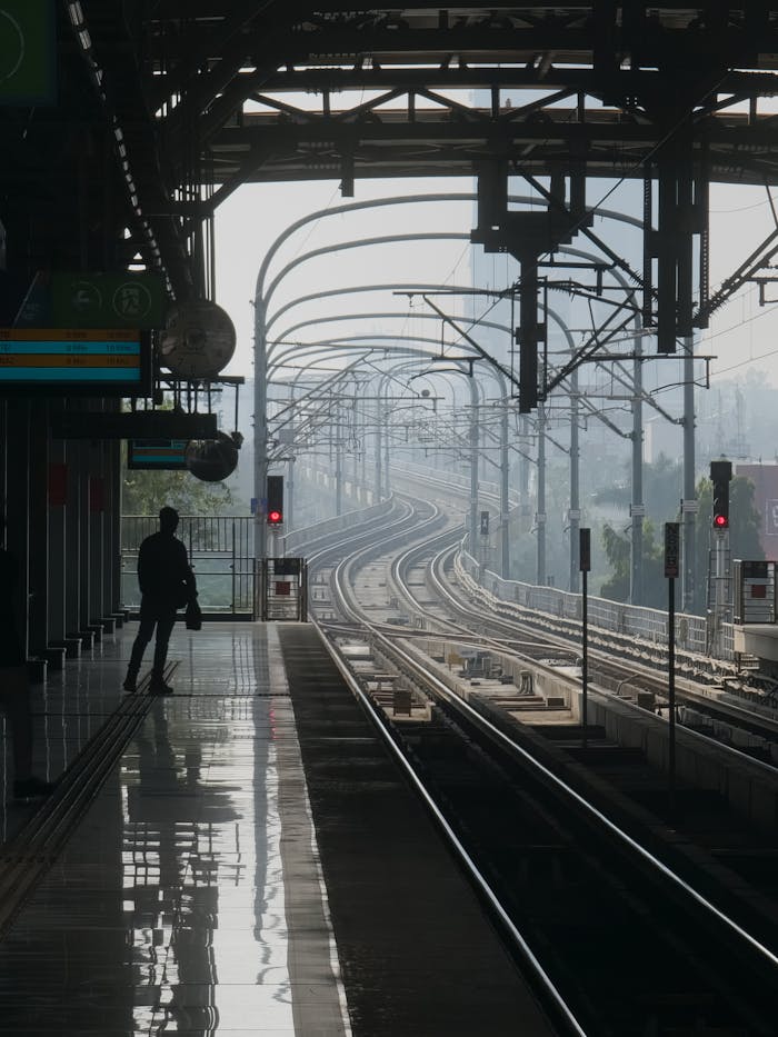 hero-img-02 Silhouetted figure at a train station with curving tracks in an urban setting, creating a sense of anticipation.
