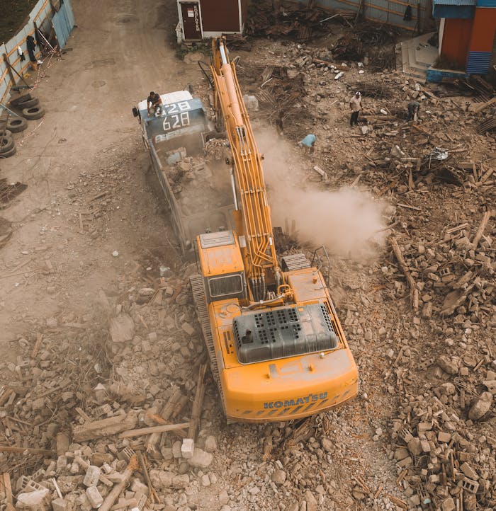 services-02 Aerial view of an excavator loading debris at a construction site with workers nearby.