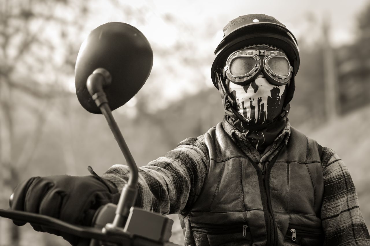 Monochrome portrait of a masked motorcyclist in protective gear set outdoors.