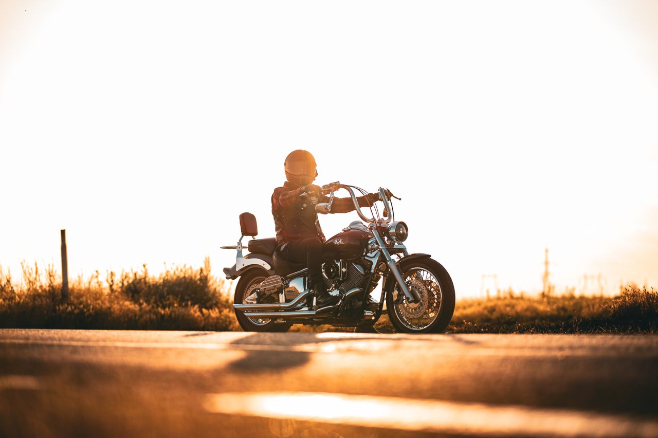 A motorcyclist in a helmet rides along a sunlit road at sunset, symbolizing freedom.
