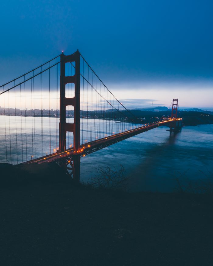 Magnificent scenery of cars driving on modern suspension bridge crossing river against cloudless evening sky